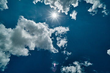 Sunny blue sky background with clouds and sun and sunny flare. Bright sun and long diverging rays in the upper center of the frame.