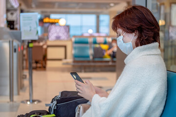 Girl in antiviral mask in the airport and looks at her smartphone. Side view, copy space.