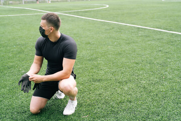 An athlete in a medical mask puts on disposable gloves. The concept of strength training alone in the fresh air.