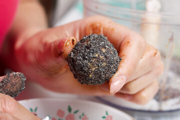 A woman is holding a dried fruit candy in her hand. Balls of prunes, dates and coconut. With a sprinkle of black sesame powder.