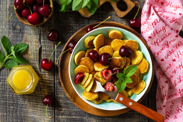 Tiny pancakes trendy food. Mini pancakes with cherries and honey on a rustic wooden table. Top view flat lay background.