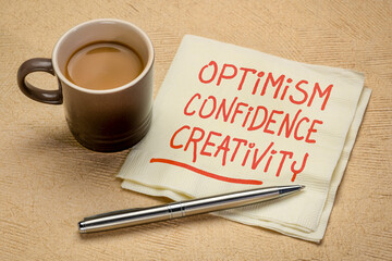 optimism, confidence, creativity inspirational handwriting on a napkin with a cup of coffee, career, lifestyle and personal development concept