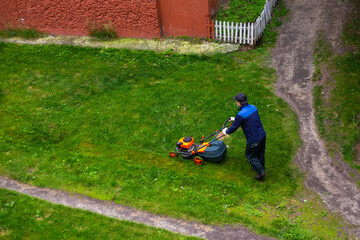 worker mows grass with a mower in the backyard of a house