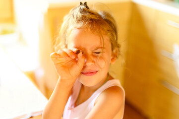 a cute happy little six year old kid girl with a black currant berry in her hand in a rustic home interior and warm sunlight pouring out of the window. flare