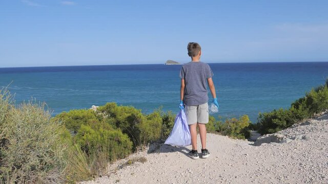 Nature cleaning, stop plastic, environmental concept. Volunteer kid raises and throws plastic garbage in the bag for recycle near the sea at sunny day