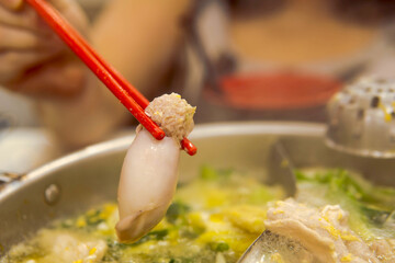 Hand holding chopsticks to pick squid  from hot pot. Food concept with gourmet Japanese Shabu Shabu, Sukiyaki cuisine.

