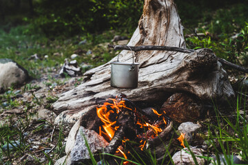 Kettle hanging over fire. Cooking food at fire in wild. Beautiful big log burns in bonfire close-up. Survival in wild nature. Wonderful flame with caldron. Pot hangs in flames. Campfire background.