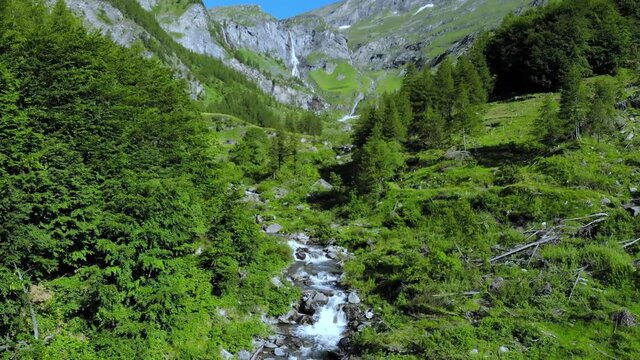 Aerial: drone flying over scenic high waterfall lush green valley and mountain stream on the italian Alps. Tourism destination hiking outdoors activity. Pis waterfall near Torino, Piedmont, Italy