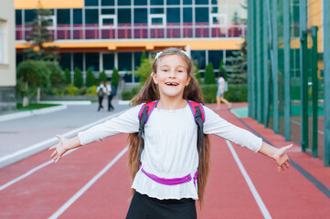 Obraz premium little smiling girl in school uniform with backpack outside