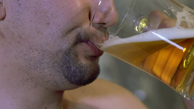 Untidy. unshaven man drinks beer from a transparent mug at home