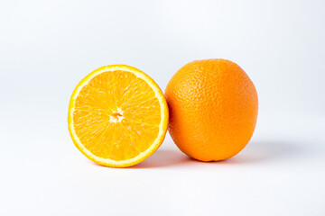 Oranges on a white background. One orange is whole, the other is cut in half. Tropical fruits