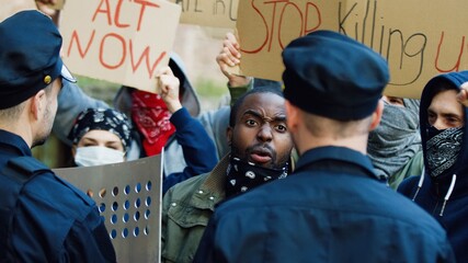 Young African American guy protester screaming and shouting at policemen at demonstration for human...