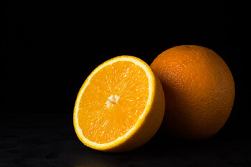 Oranges on a black background. One orange is cut in half, the other is whole. Tropical fruits.