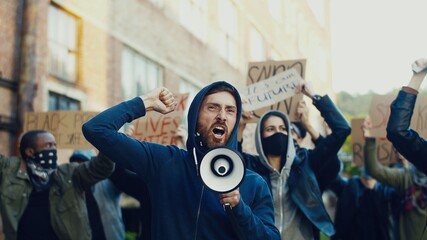 Caucasian young handsome guy protesting in middle of multiethnic crowd of protesters and screaming...