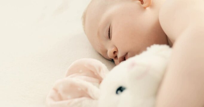 The baby is sleeping in the crib. A peaceful baby in a diaper, lying on a bed and sleeping in a room with its stuffed rabbit
