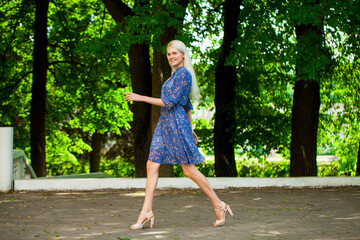 Portrait of a young blonde woman in blue dress walking in summer parkpark