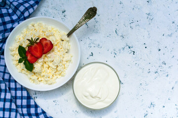 A plate of cottage cheese and sour cream decorated with strawberries on a blue background. Copy space