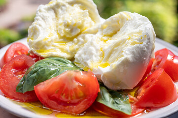 Ingredients for vegetarian caprese salad, buffalo mozzarella cheese, fresh basil, tomatoes, olive oil. Italian food served outdoor on terrace