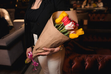 Beautiful young woman holding a bouquet of fresh red yellow white tulips , beautiful colourful blossoming flowers . Restaurant nightclub background, 8 March holiday concept