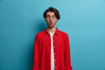 Half length shot of embarrassed shocked hipster guy with trendy hairstyle, gasps from wonder,...