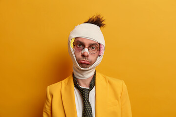 Sad displeased man with gloomy expression looks distressed at camera, has bad mood after accident...