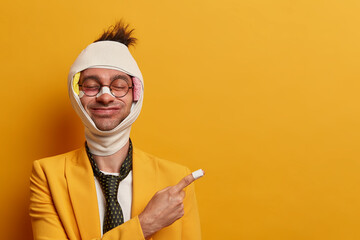 Cheerful man with funny face expression, closes eyes, recovers after injury, has abrasions and...