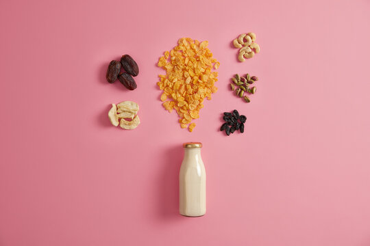 Continential Breakfast. Spilled Off Dry Cereals With Dried Apples, Dates, Cashew, Pistachio Around Bottle With Milk. Pink Background. Healthy Proper Nutrition. Ingredients For Making Quick Snack