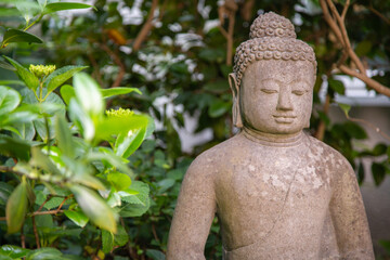 Breast-section of a meditative Buddha stone sculpture in the lotus seat in a garden in front of green bushes