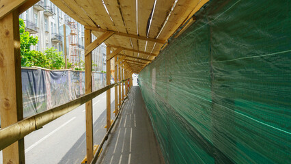 Protective canopy over the sidewalk and fence near a house under construction.