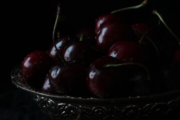 Fresh sweet ripe cherries on rustic plate on black background. Close up.