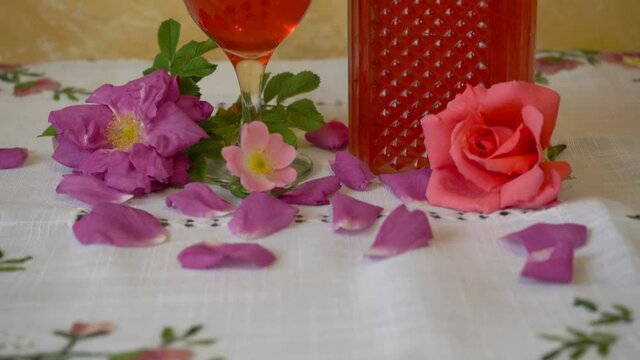 rose liqueur in a glass,on the table a glass of red liqueur with rose petals and a bottle, wine production at home