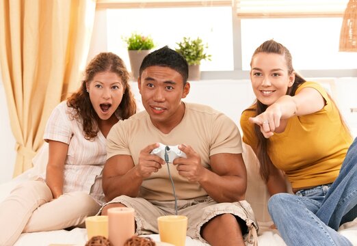 Group of happy young friends sitting on sofa at home having fun together playing video game. 