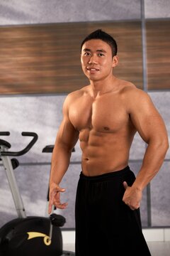 Portrait of shirtless muscular asian man exercising looking at camera in gym. 