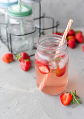 Strawberry lemonade with rosemary and ice in mason jar on a gray concrete table. Seasonal food concept. Summer harvest time