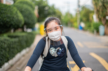 Back to school. asian child girl wearing face mask with backpack biking a bicycle and going to school .Covid-19 coronavirus pandemic.New normal lifestyle.Education concept.