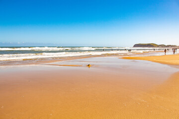 Fototapeta na wymiar Reflexo do céu na areia molhada pelas ondas do mar em um dia quente na praia de Torres, a mais bela praia do Rio Grande do Sul, Brasil
