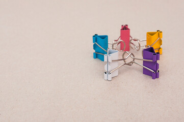 Five binder clips of different colors on a gray paper background making star figure by holding hands, selective focus