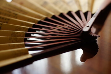 open yellow fan with brown chinese characters on the table, closeup, side view.