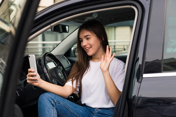 Fototapeta na wymiar Young woman waving during a video call with a mobile phone in a car