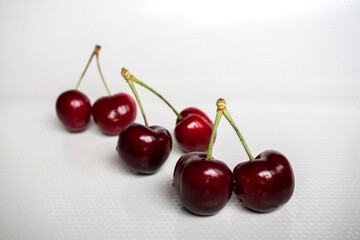 Three pairs of sweet red cherries arranged in a row on a white background. Food and drink concept