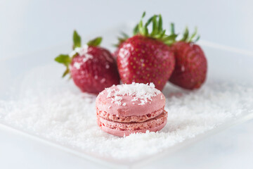 Pink french traditional macaroon and red ripe strawberries on white plate with cocoflakes background. Close up