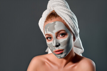 Beautiful woman with clay mask on a gray background.