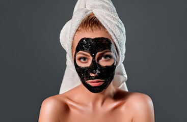 Beautiful woman with black peel-off mask on a gray background.
