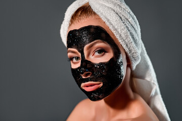 Beautiful woman with black peel-off mask on a gray background.