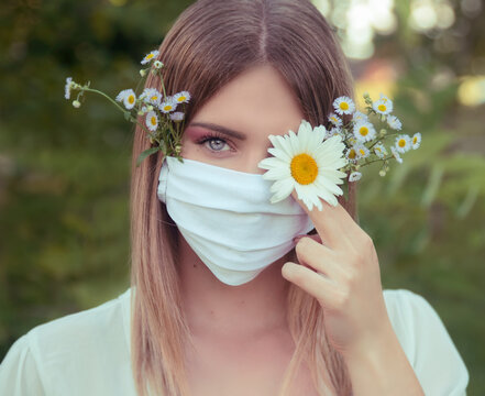 Young woman wears protective mask outdoors and holding flower