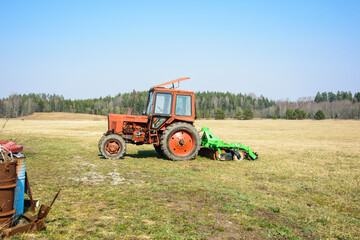 A red tractor stands on a field in early spring.