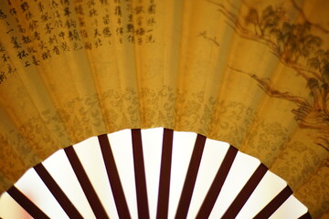 yellow fan with brown chinese characters on it, white background, closeup.