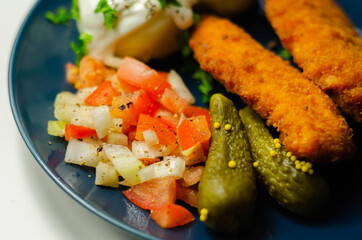 Breaded and herbed chicken breast fillet served with mashed potatoes,  tomato salad with onions and gherkin