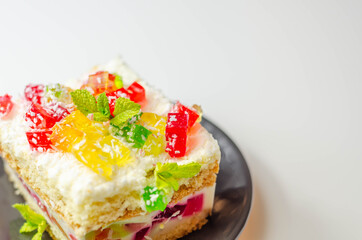 A portion of cream cake with pieces of colorful jelly and sprinkled with coconut flakes