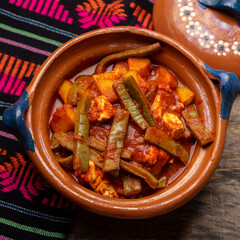 Mexican potato and nopal cactus stew with red sauce on wooden background